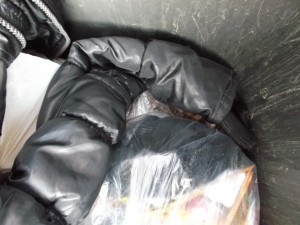 Ein nutzlos gewordener Ärmel hat sich seinem Schicksal im Müll offensichtlich ergeben und schmigt sich nun zwischen einem Küchenmüllbeutel und der Wandung der Mülltonne.