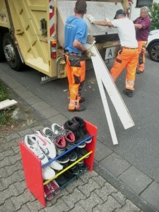 Während der Pressmechanismus mit Leichtigkeit die Sitzfläche des Sofas zermalmt, hält der eine Müllwerker das berstende und bebende Möbel fest, damit es nicht als Trümmerhaufen wieder auf die Straße plumpst.