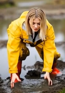Vrouw geel regenjack rode laarzen smeert meer modder.jpeg